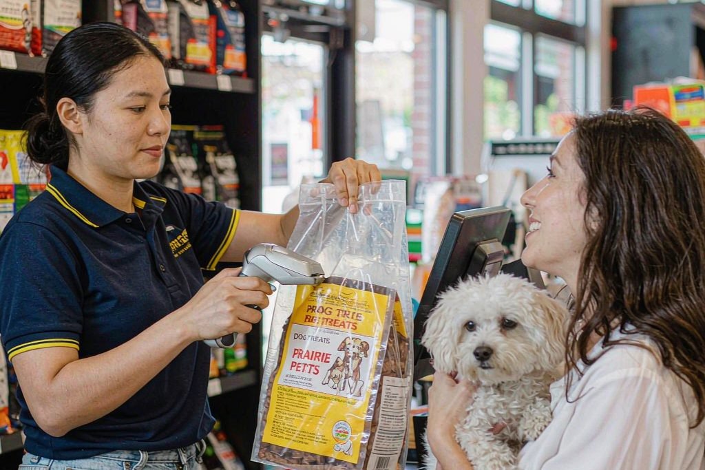 An assistant serving a customer holding a small white dog at a pet shop counter